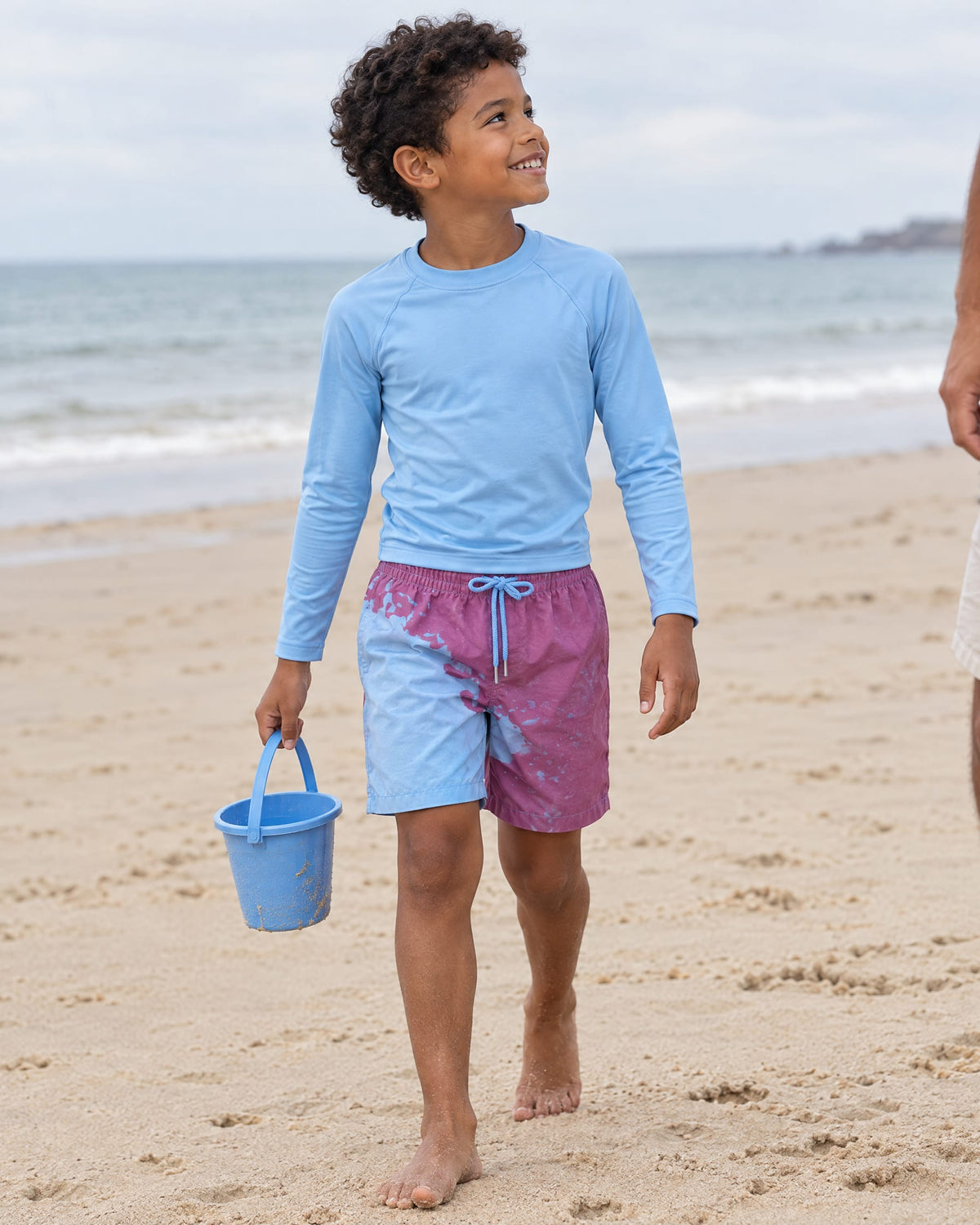 Boy with a bucket on the beach in Shift kids' Purple to Blue swim shorts