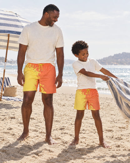 Dad and son with a beach towel in matching Shift Orange to Yellow swim shorts
