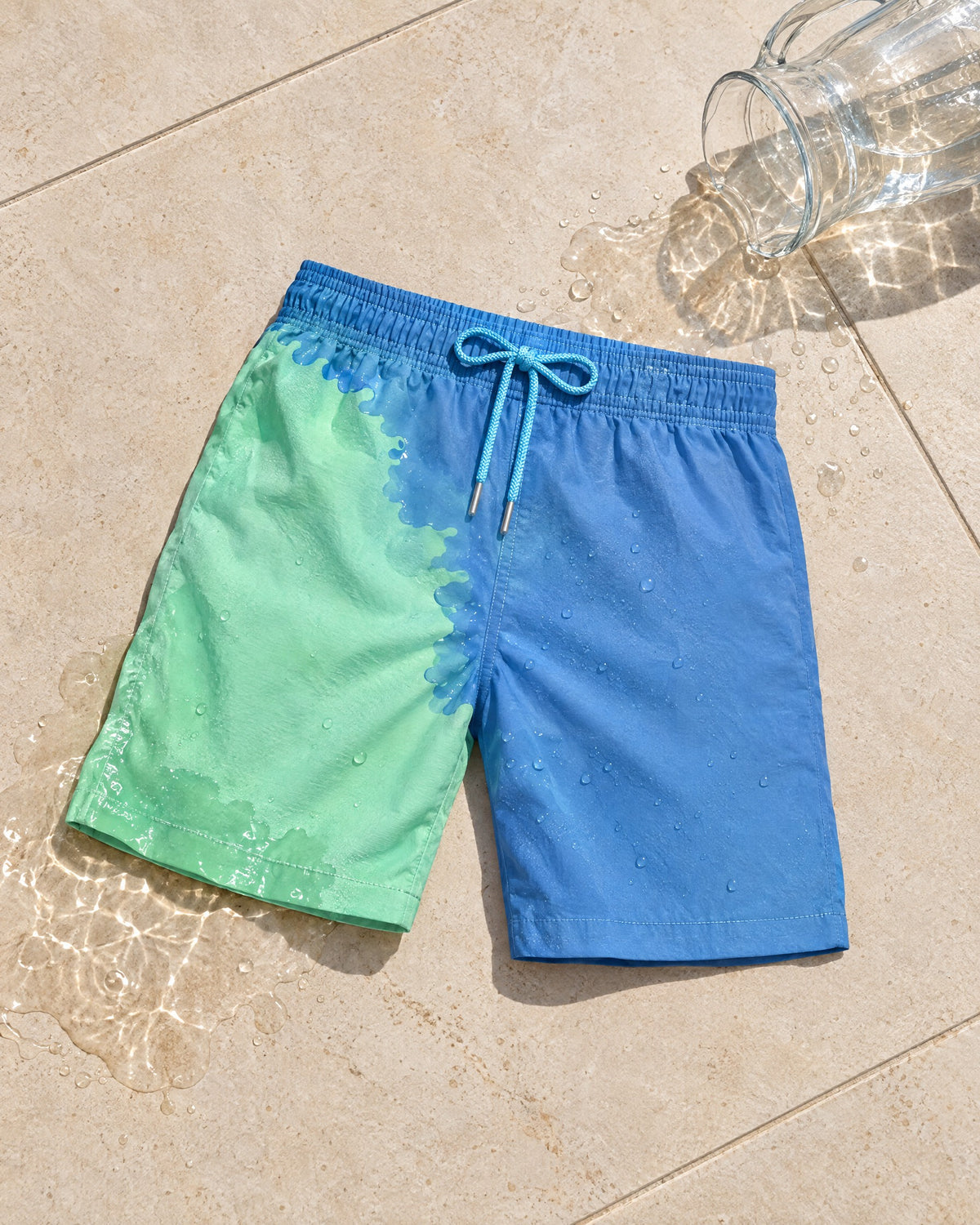 The Original colour-changing swim shorts in Blue to Green next to a spilled water jug