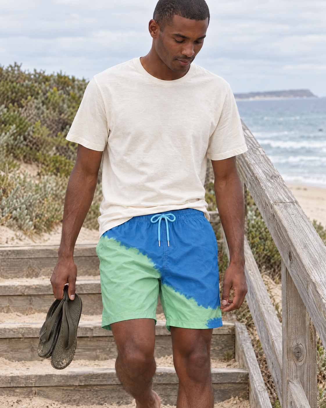 Man walking down beach stairs in Shift Blue to Green swim shorts