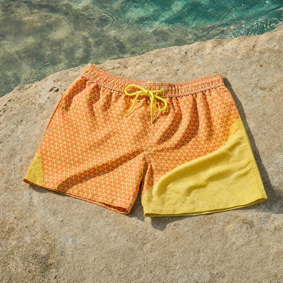 Shift Geometric colour-changing swim shorts, Orange to Yellow, on coastal stone