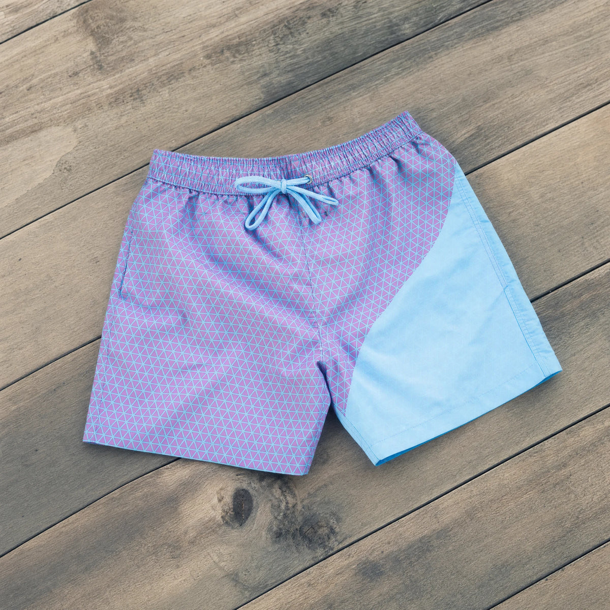 Shift Geometric colour-changing swim shorts, Purple to Blue, on a timber deck