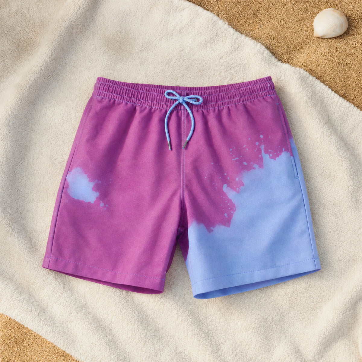 Shift kids' colour-changing swim shorts, Purple to Blue, on a beach towel